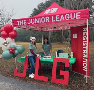 Two members stand up a red Junior League of Gainesville tent while volunteering at our community holiday event.